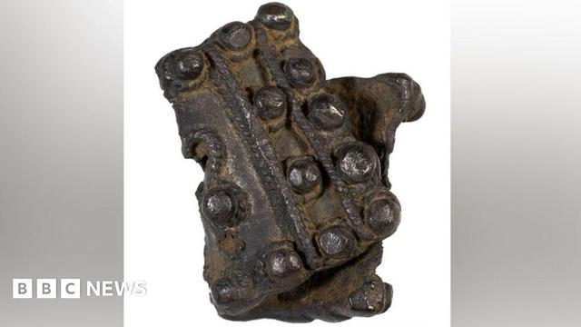 An early medieval silver brooch. It is folded in half.  The brooch is divided by strands of corded wire. It has raised solid bosses running along its width. 