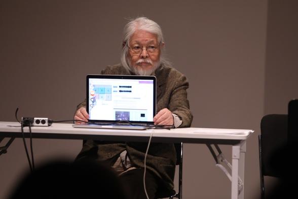An elderly Asian man holding up a laptop screen to an audience. An elderly Asian man holding up a laptop screen to an audience.