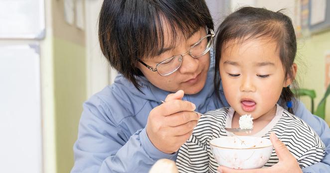 Woman helping a small child spoon rice from a bowl