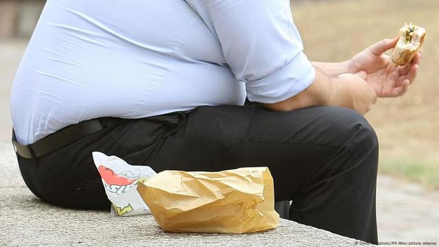 Ein übergewichtiger Mann sitzt auf einer Bank und isst