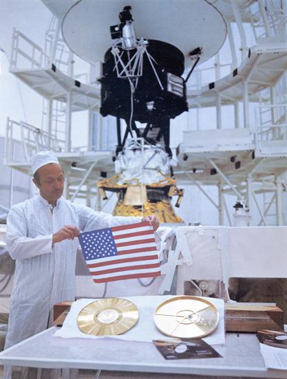 With Voyager 2 in the background, John Casani holds a small U.S. flag
