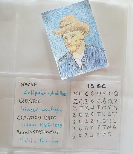 Three paper cards, one with an artwork, one with metadata and one with the header ISCC and letters and numbers. The two latter are in a binder.