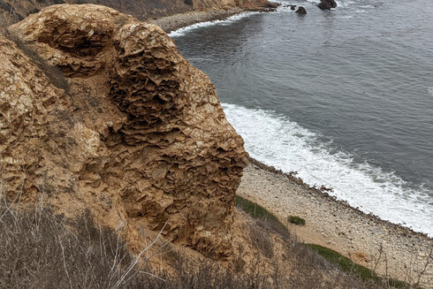 A large rock at the top of a cliff, looking down to the ocean, that looks like a stack of really thin layers that have been scrunched and folded and eroded differently.
