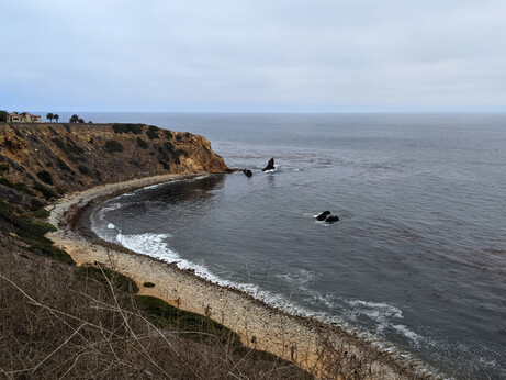 A cove on a gloomy day with rocky shore, high bluffs, and a few rocks out in the sea.