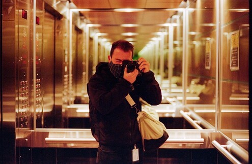 Photo of a man taking a photo of himself in an elevator, orthogonal to one side of the elevator, and both sides of the elevator are mirrors. Created a background reflection to infinity.