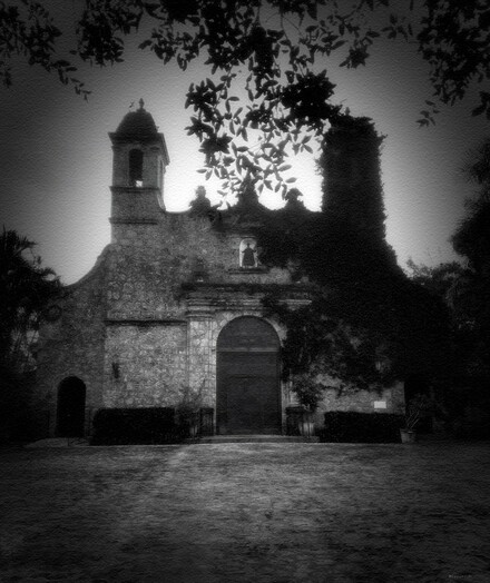 Old coral rock church half covered by vines