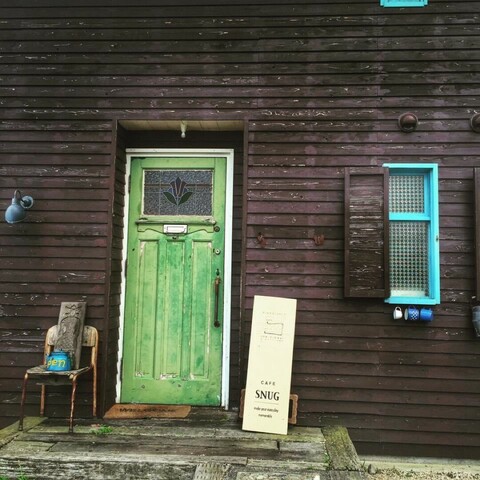 Dark brown wooden wall with faded out green door and light blue window frame