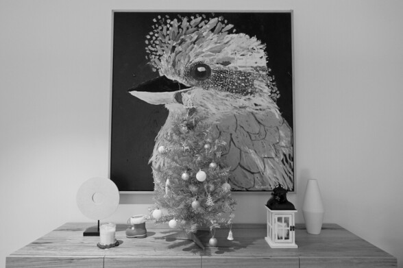A small christmas tree and other christmas ornaments on a sideboard, in front of an oil painting of a kookaburra