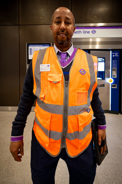 A photograph of a member of staff in their new Elizabeth Line-branded uniform and high-vis orange jacket.