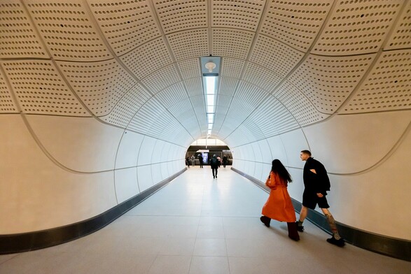 A photo of a new tunnel for the Elizabeth Line in London with two passengers walking on the right towards the platforms.