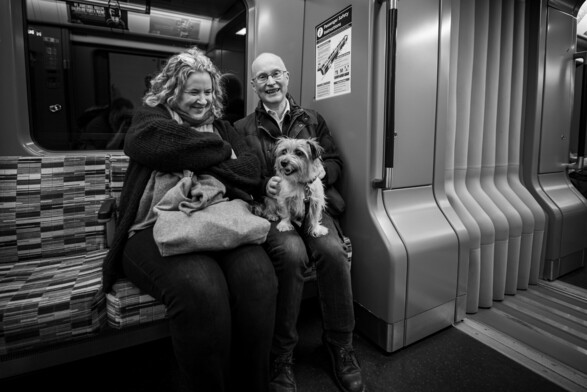 A photograph of a couple sat on a new Elizabeth Line train with their dog on the man's lap.
