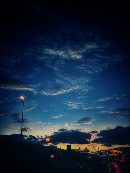 Dawn sky. Only the horizon part started turning orange and the rest of the sky is still dark. Traffic is already started and there’re lines of cars’ taillights. Orange street lights stand out in still dark sky. 