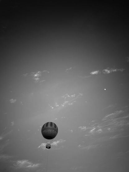 Balloon floating in the evening sky. There’s a tiny half moon upper corner of the sky