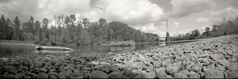 A170 degree panoramic pinhole photo taken from ground level along a rocky stream shoreline.