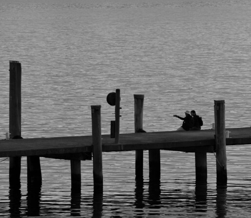 A couple sitting on the edge of a jetty at Strahan, Tasmania. They are mid-selfie