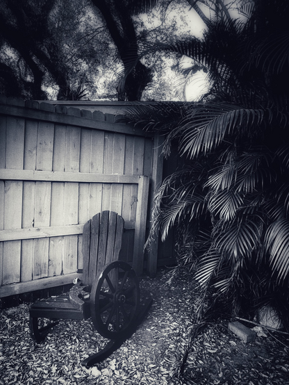 A wooden chair left on the corner of the street by the wooden wall. Arm and legs are broken