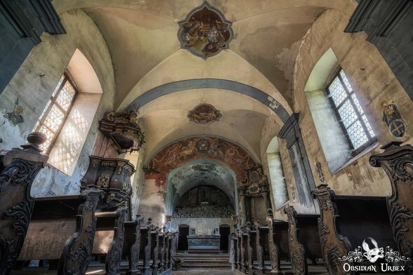 Abandoned church in Austria. Gothic style with carved dark wooden pews. There is a red mural above the altar, and a dark wooden pulpit