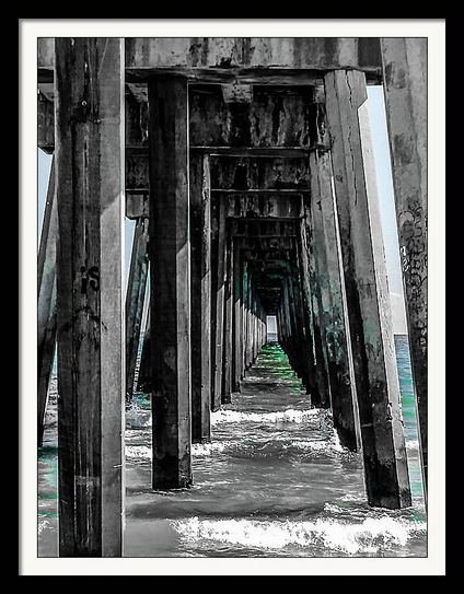 Phot view from the beach looking under the pier with waves rolling toward the shore. Selective coloring process with hints of aqua on black and white
