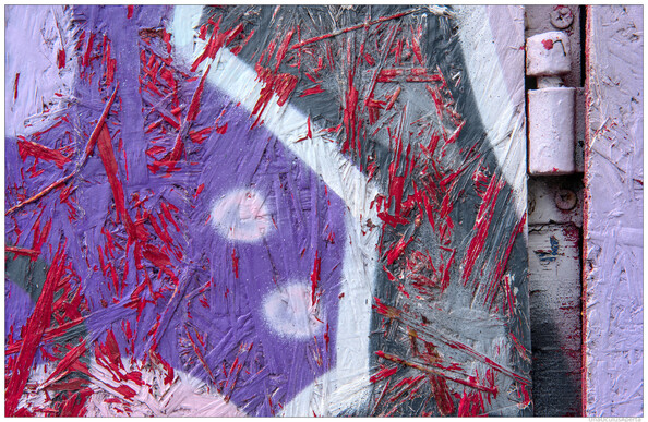 A colour photograph, mainly pink, purple and grey, of a recessed hinge supporting a OSB woodflake board door.