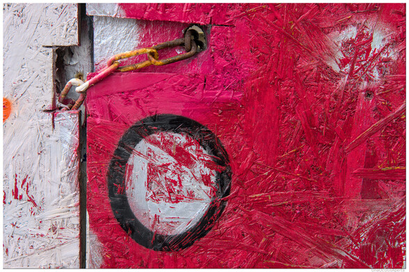 A colour photograph, mainly red  & white, of a small rusting chain keeping closed together two OSB - Woodflake Board doors.