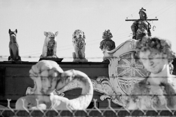 A concrete dog, a pig and a lion stand guard behind a barbed wire fence.