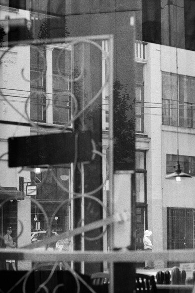 Pedestrians wait for the bus as viewed through a cafe window.