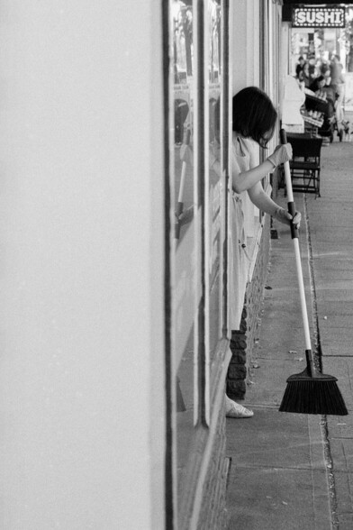 A shop owner sweeps the sidewalk in front of her storefront.