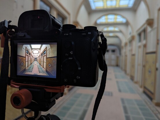 Camera on tripod showing photo preview. Photo of a long hallway with tiled walls and floor, it is an old spa