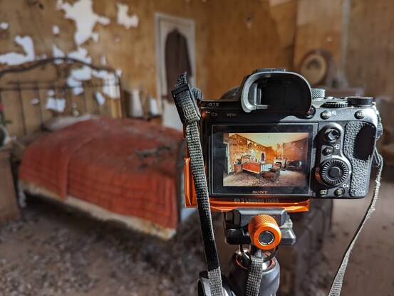 Camera on tripod showing photo preview. Photo of a bedroom with an old red bed