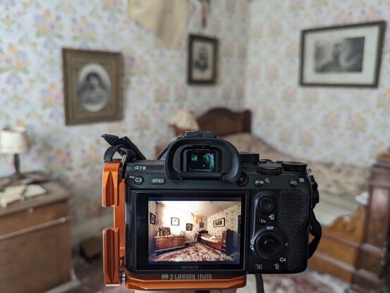Camera on tripod showing photo preview. Photo of an old bedroom with wooden bed, there are framed photos on the wall