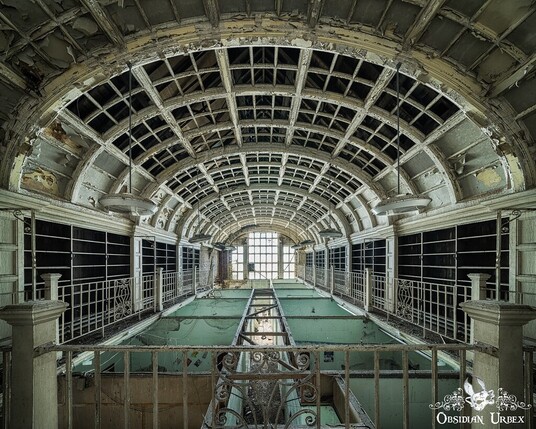 old library. the roof is vaulted and the metalwork is bare, the panels have fallen. this photo is on the mezzanine floor looking over the reading hall which has mint green dividers