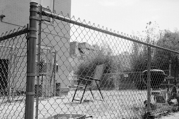 A lawn chair and barbecue await use behind a fence.
