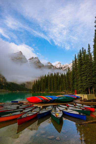 Colorful canoes on Moraine Lake, Banff National Park Alberta Canada reflecting on the lake on a foggy autumn morning with snow covered Rocky Mountains peaks and pine trees in the background 
Captured by Komeil Karimi
