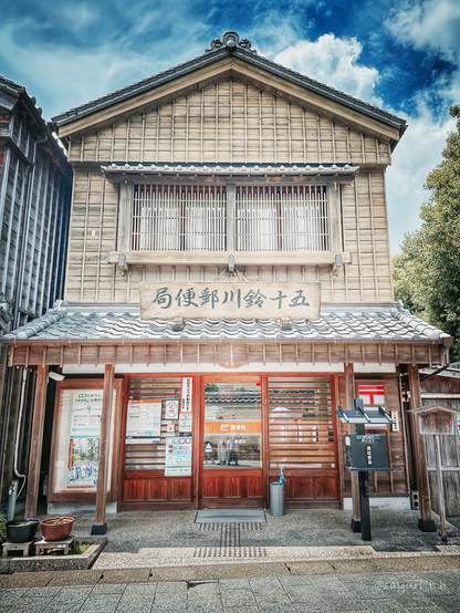 Two stories wooden post office building with black tile roof. 