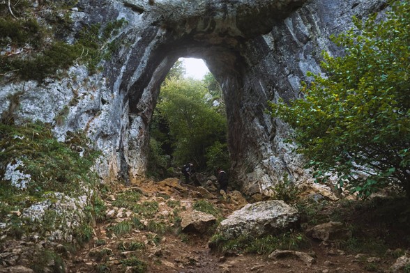 Looking up at a natural archway with daylight bleeding in underneath it.