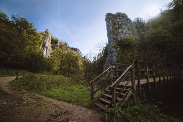 Nearby a footbridge crosses the river whilst a huge white rocky spire rises above the valley floor, with another in the distance facing it, catching the light.