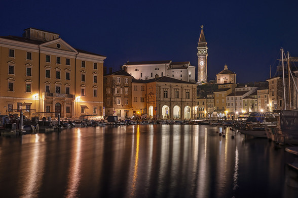 Early morning in Piran, Slovenia with the lights of buildings reflecting in the harbor below. 