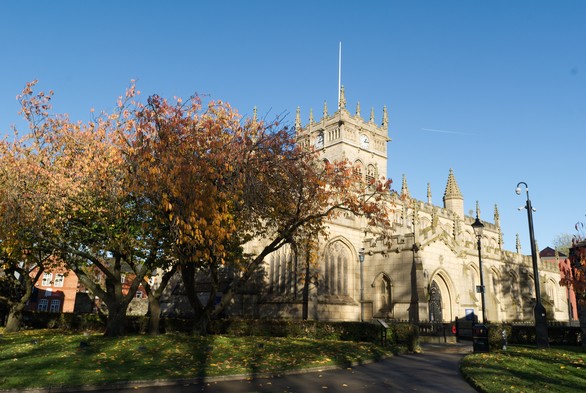 A colour digital photo of Wigan Parish Church with some autmn colour on the trees outside.