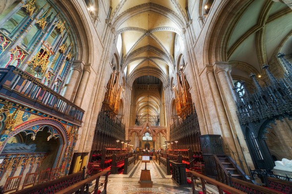 The image depicts a large, ornate cathedral with a high ceiling and a long, narrow interior. The cathedral is filled with numerous pews, arranged in rows, and a large number of books are placed on the pews. The books are of various sizes and are spread across the cathedral, creating an atmosphere of learning and spirituality. The cathedral's architecture and design make it an impressive and majestic space for worship and reflection.