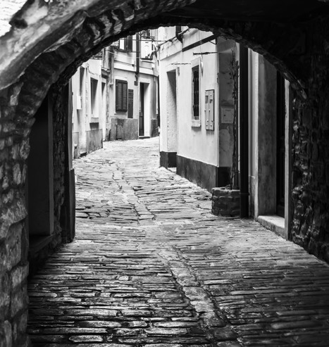 One of the old town streets of Piran Slovenia, framed by a arched tunnel across the street; processed in black and white.  