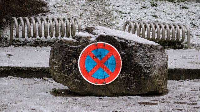 Ein Stein, auf den ein absolutes Halteverbot montiert ist. Das Verkehrszeichen reflektiert Licht und erscheint leuchtend