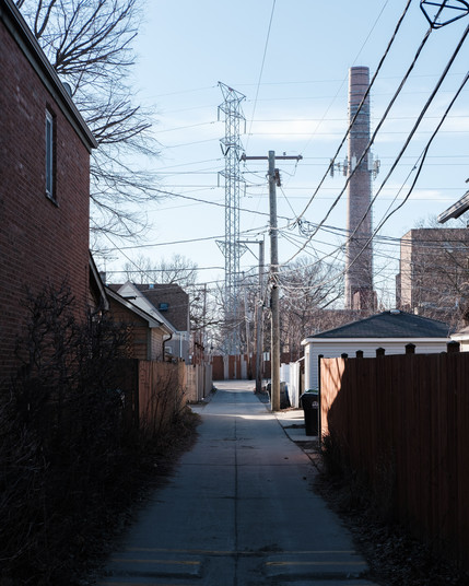 A concrete paved alley extends towards a smoke stack and high tension powerline tower.