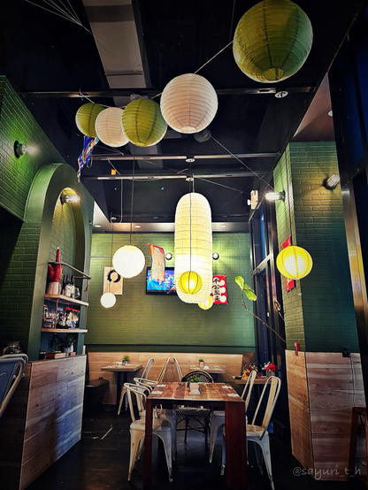 Empty tables and chairs inside of the restaurant. Green wall and lots of lantan-looking lamps 