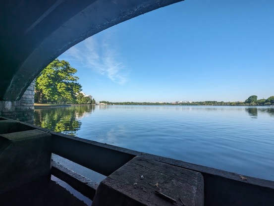 Washington DC tidal basin as seen from under a bridge. Jefferson memorial is behind trees to the left. Water is completely calm and blue sky with some faint white clouds