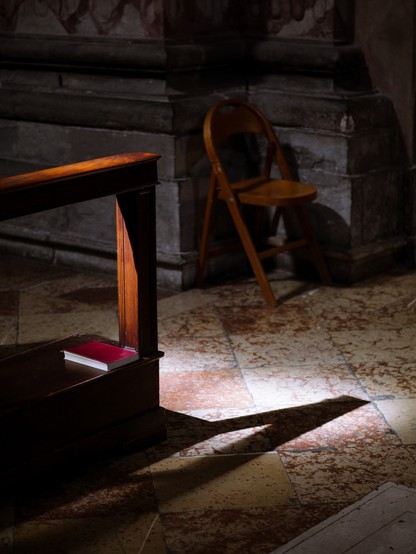 A book on a bench is illuminated by sunlight filtering through a window. The place looks like a church.