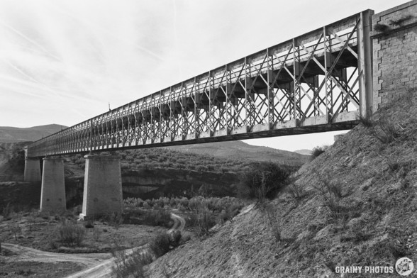 A black-and-white film photo of a steel truss viaduct on the via Verde. 