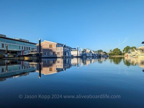 Floating house and boats in Gangplank Marina at sunrise reflecting in water with blue sky