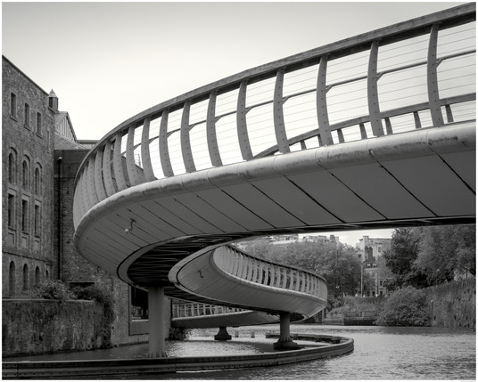 A close in and underneath black and white photograph of part of Castle Bridge. An S-Curved Pedestrians and Cyclists Bridge joining Castle Park to Finzel Reach in Central Bristol. 
The buildings on the left are what used to be The Bristol Brewery, Georges & Co. Ltd which later became 'Courages' and closed 1999.