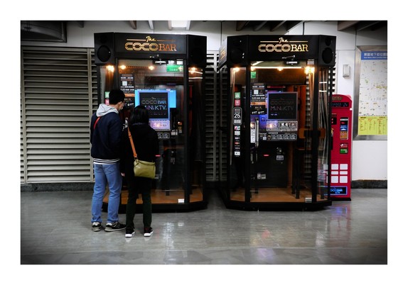 The image is a color photograph taken in Taipei, showing two individuals standing in front of two adjacent kiosks labeled 
