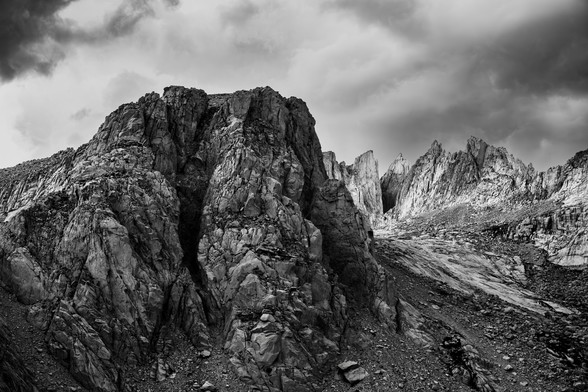 Black and white photograph of rugged mountain peaks under a cloudy sky.